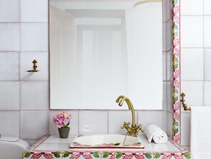 Un baño con lavamanos blanco, grifo de latón, espejo y planta en maceta.