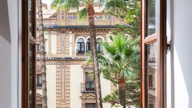 Blick durch ein Fenster eines Gebäudes, mit dem Schild "Hotel Nox" und Palmen vor der Fassade.