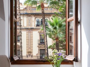 A view through a window of a building with the sign "Hotel Nox" and palm trees outside. - The house in San Fernando, overlooking the gardens of the Alcázar and the Giralda (Sevilla)