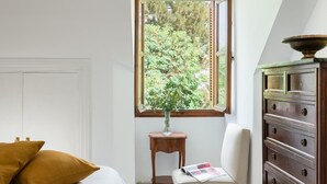 Ein Schlafzimmer mit einem Bett, einem Fenster mit Blick auf Bäume, einem kleinen Holztisch und einer Kommode.