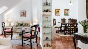 Ein geräumiges Wohnzimmer mit hohen Decken, einem Glastrennregal, einem Essbereich mit Holzsesseln und einem Marmorboden.