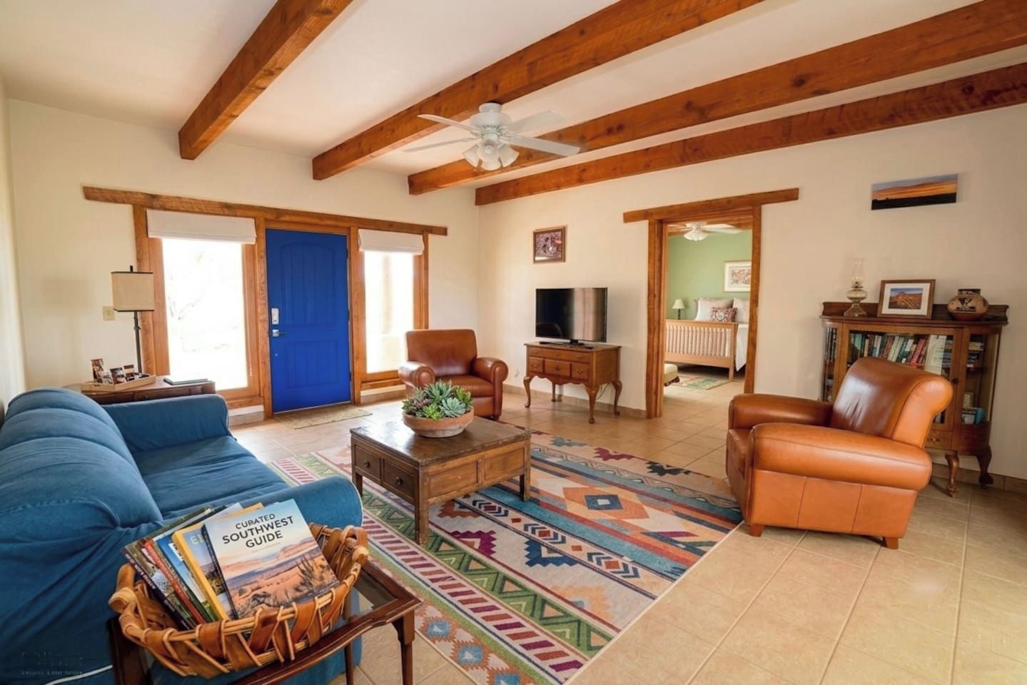 A living room with a blue sofa, a brown leather armchair, a coffee table with a plant, a television, and a bookshelf.
