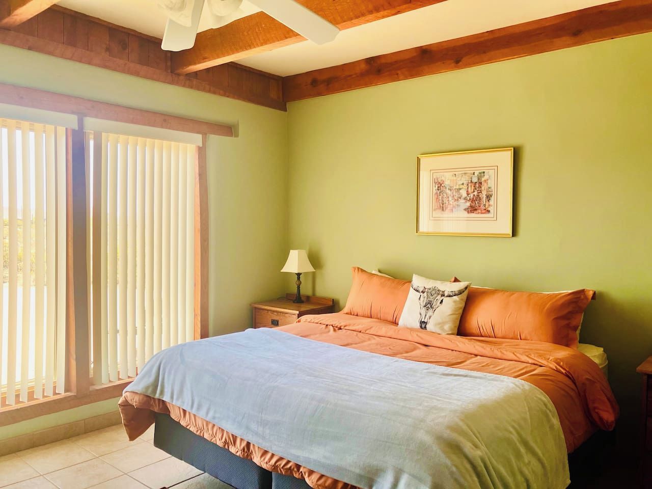 Une chambre à coucher avec un lit, une table de chevet, une lampe et une fenêtre avec des stores.