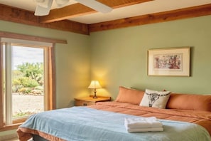 Un dormitorio con cama, mesita de noche, lámpara, un cuadro enmarcado y vistas al exterior.
