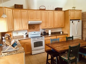 A kitchen with wooden cabinets, a stove, a refrigerator, and a dining table with chairs.