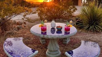 A round table with two chairs, each with a mosaic seat, set outdoors with a sunset in the background.
