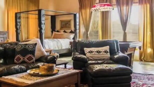 Een gezellige kamer met een houten plafond, een bed met hoofdeinde, een bank, een bijzettafeltje en een kamerkleed met dessin.