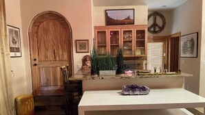 Een keuken met een houten deur, een televisie boven een houten kast en een wit aanrechtblad met een kristal erop.
