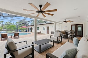 An open-plan living area with a pool, outdoor furniture, ceiling fans, and a glass-enclosed patio.