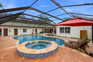 Une piscine avec un jacuzzi, des chaises longues et un patio couvert.