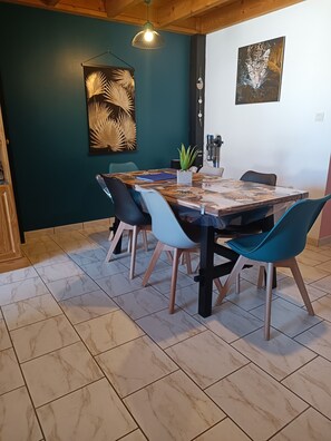 Un comedor con una mesa dispuesta para cuatro personas, sillas alrededor, una planta en maceta y obras de arte en las paredes.