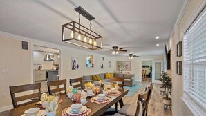 A dining area with a long wooden table set for a meal, a ceiling fan, and a kitchen in the background. - Lancaster Perfect Vacation HOME - Pool Heating Avail (Clearwater)