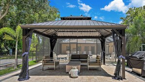 A covered outdoor seating area with a gas cylinder, benches, and a grill. - Lancaster Perfect Vacation HOME - Pool Heating Avail (Clearwater)