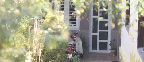 Un étroit sentier mène à une maison avec une porte et des fenêtres blanches. Un scooter est garé devant l’entrée.