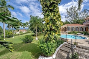 Un resort tropical con piscina, exuberante vegetación y una casa grande con techo rojo.