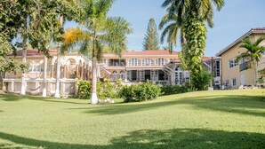 A large, multi-story building with a red-tiled roof, surrounded by lush greenery and palm trees. - Music Mansion (Montego Bay)