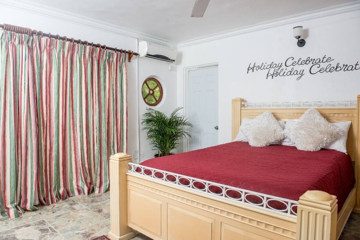 A bedroom with a bed, curtains, a wall clock, a potted plant, and a decorative wall sign.