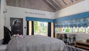 Un dormitorio con una cama grande, un escritorio y una silla. Se ve un ventanal con vistas a la vegetación.