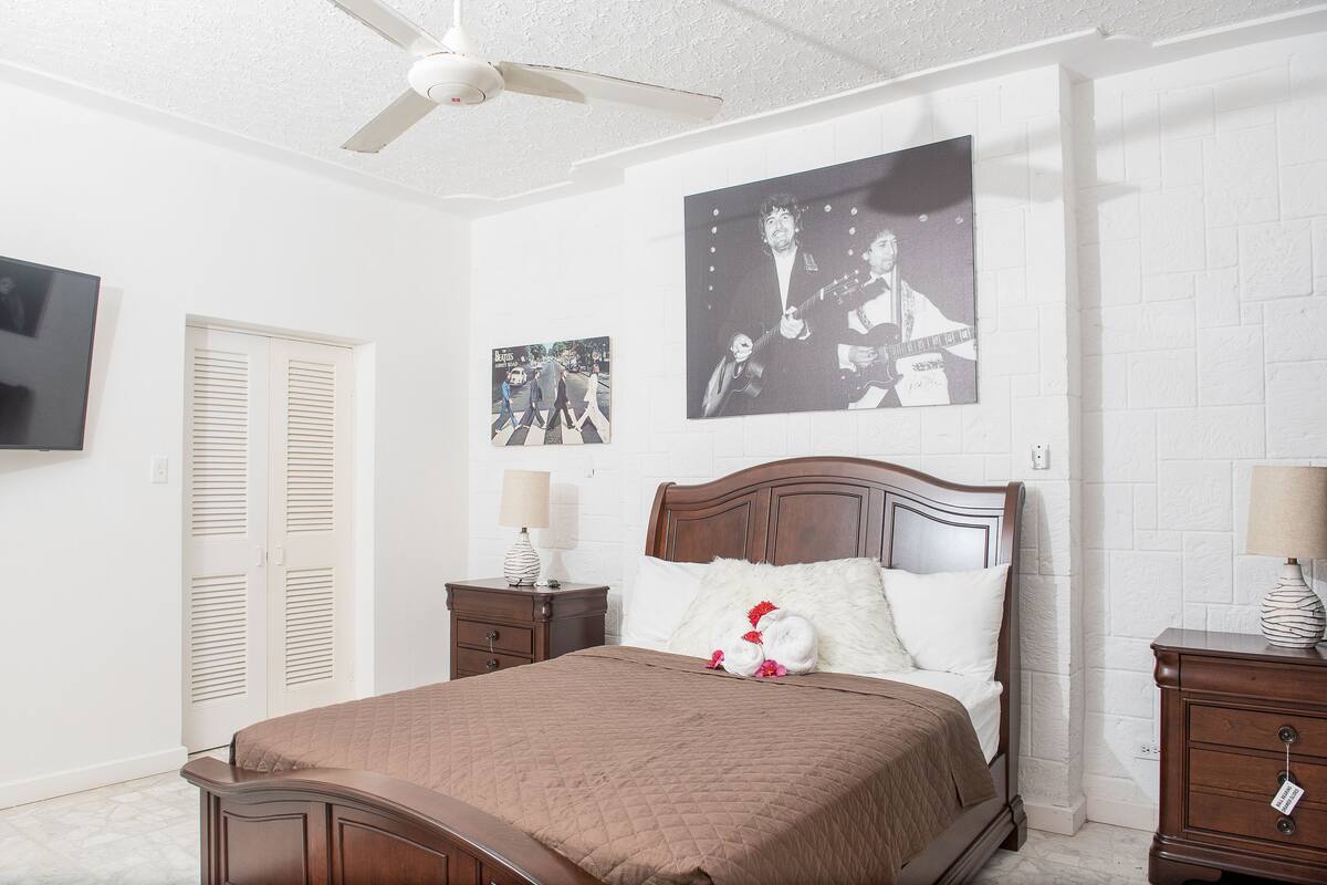 A bedroom with a bed, a nightstand, a wall-mounted TV, and a ceiling fan.