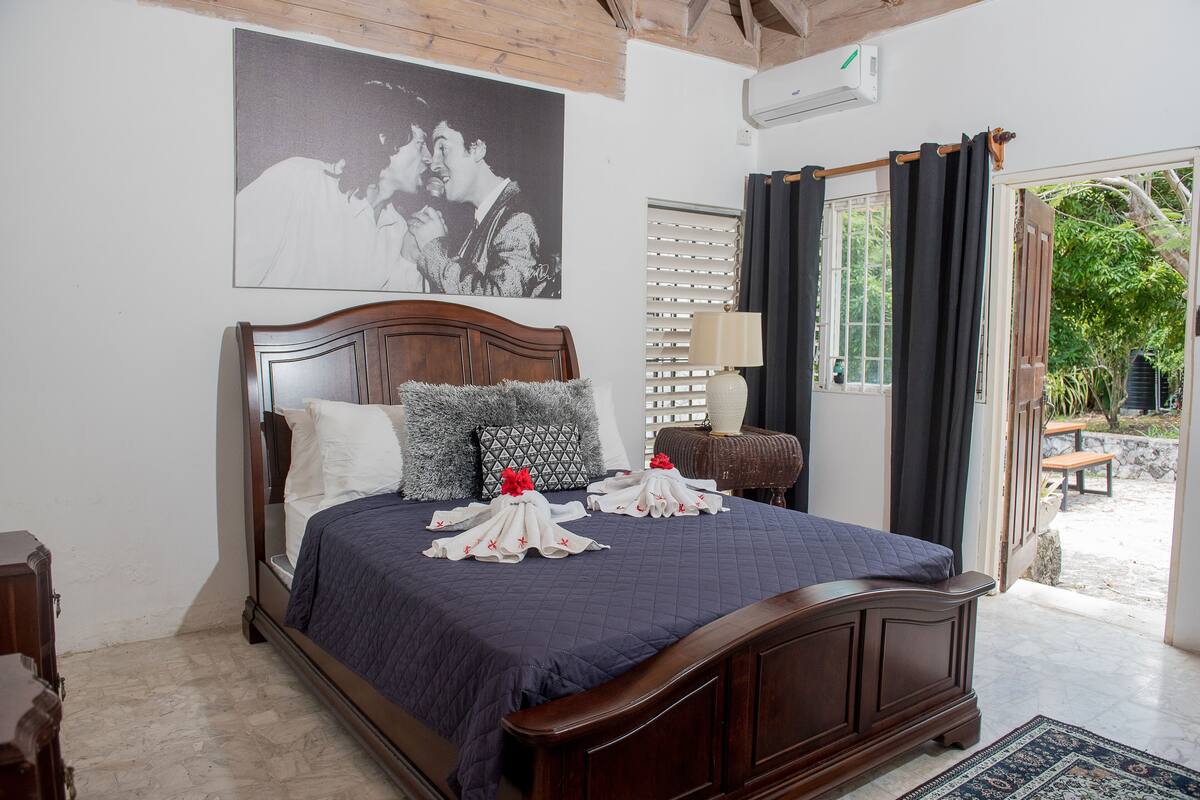 A neatly made bed with a dark blue bedspread and pillows, a wooden headboard, and a large framed picture on the wall.
