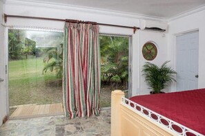 Un dormitorio con cama, puerta corrediza de vidrio que da a un jardín, planta en maceta y un reloj de pared.
