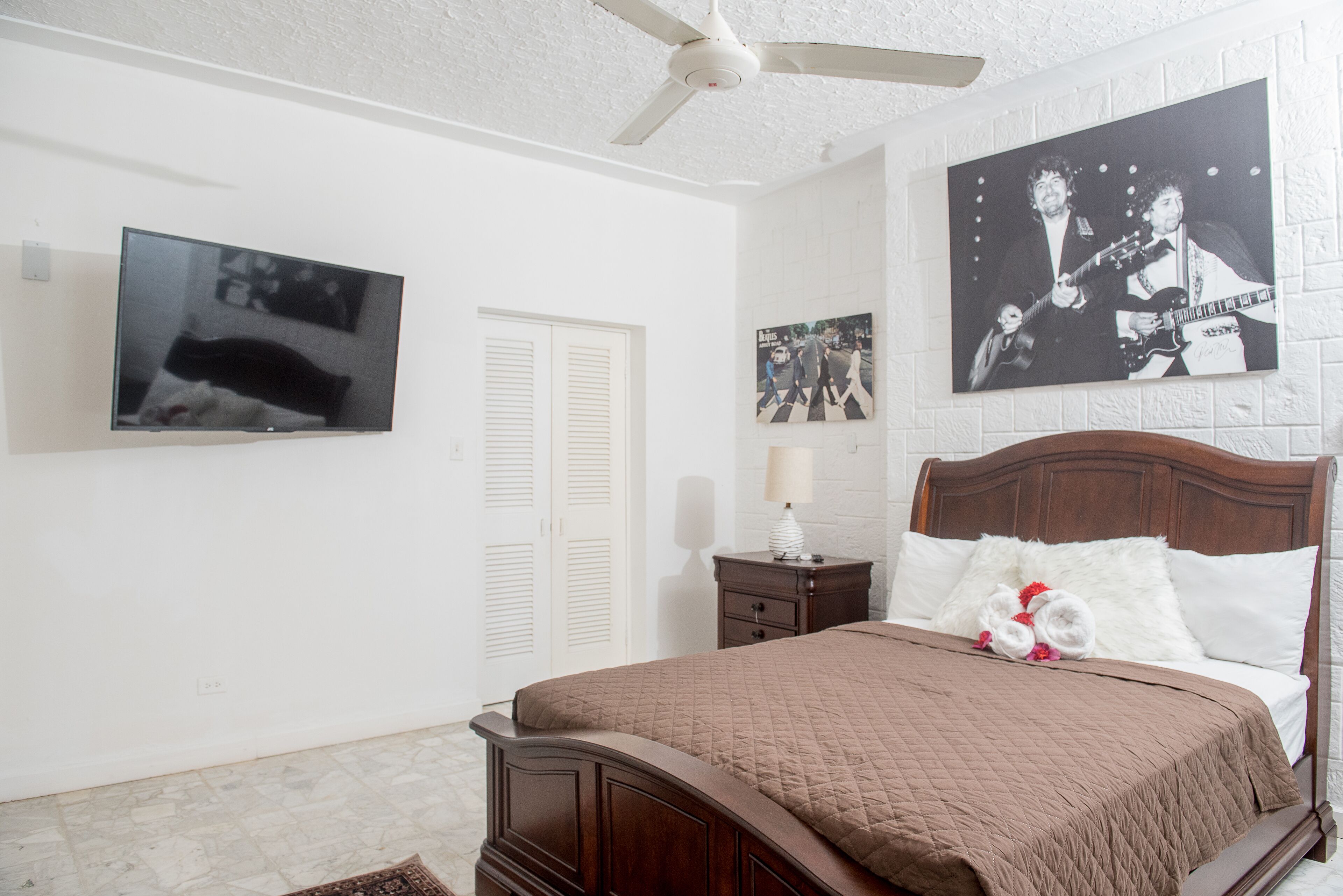 A bedroom with a bed, a television, and a ceiling fan.