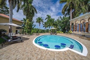 A swimming pool with lounge chairs and umbrellas, surrounded by palm trees and a stone patio. - Music Mansion (Montego Bay)