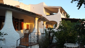 A white building with a covered porch, stone steps, and a small garden area.