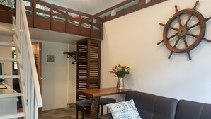 Een gezellige zithoek met een leren bank in bruin, een houten tafel met stoelen, een decoratieve scheepsschijf en een trap naar een slaapzolder.