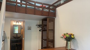 Een kamer met een stapelbed, een houten tafel met een bloemenvaas, een bankje en een deur naar een badkamer.