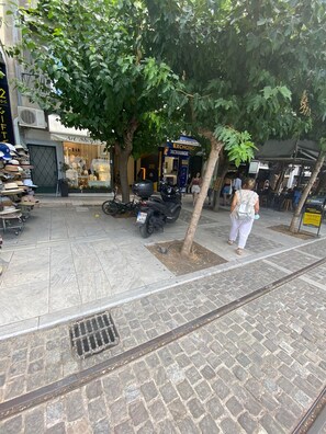 Una calle con aceras arboladas, una motocicleta estacionada en la banquina y una mujer caminando.