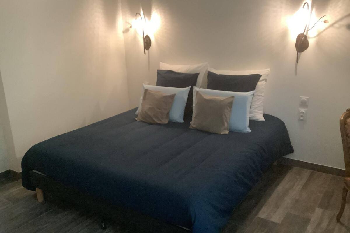 Une chambre à coucher avec une couvre-lit bleu foncé, de nombreux coussins et des appliques murales.