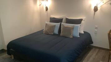 Une chambre à coucher avec une couvre-lit bleu foncé, de nombreux coussins et des appliques murales.