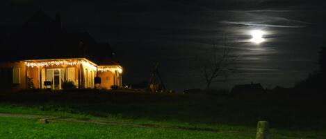 Una casa con un porche iluminado y una luna grande en el cielo.