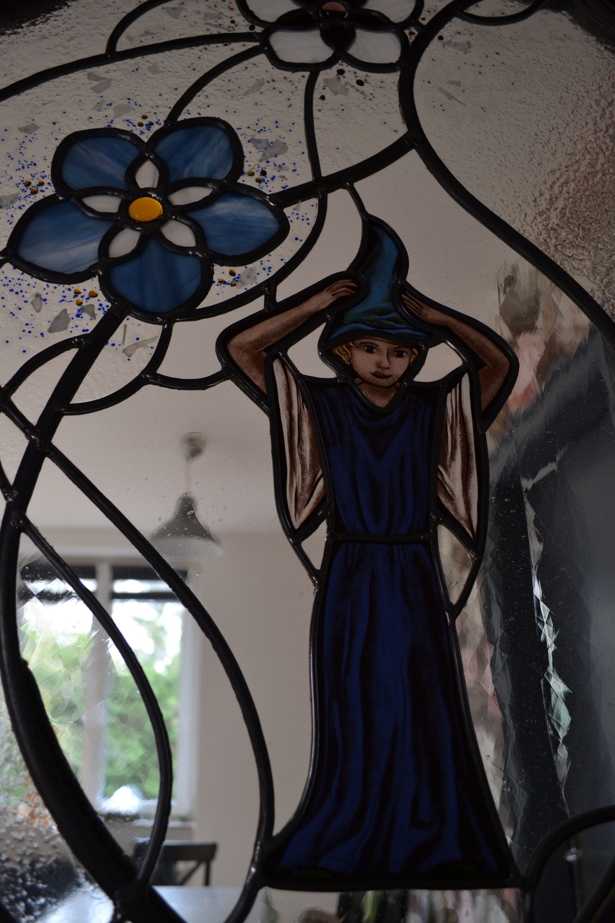 A stained glass window with a blue flower and a figure in a blue dress.
