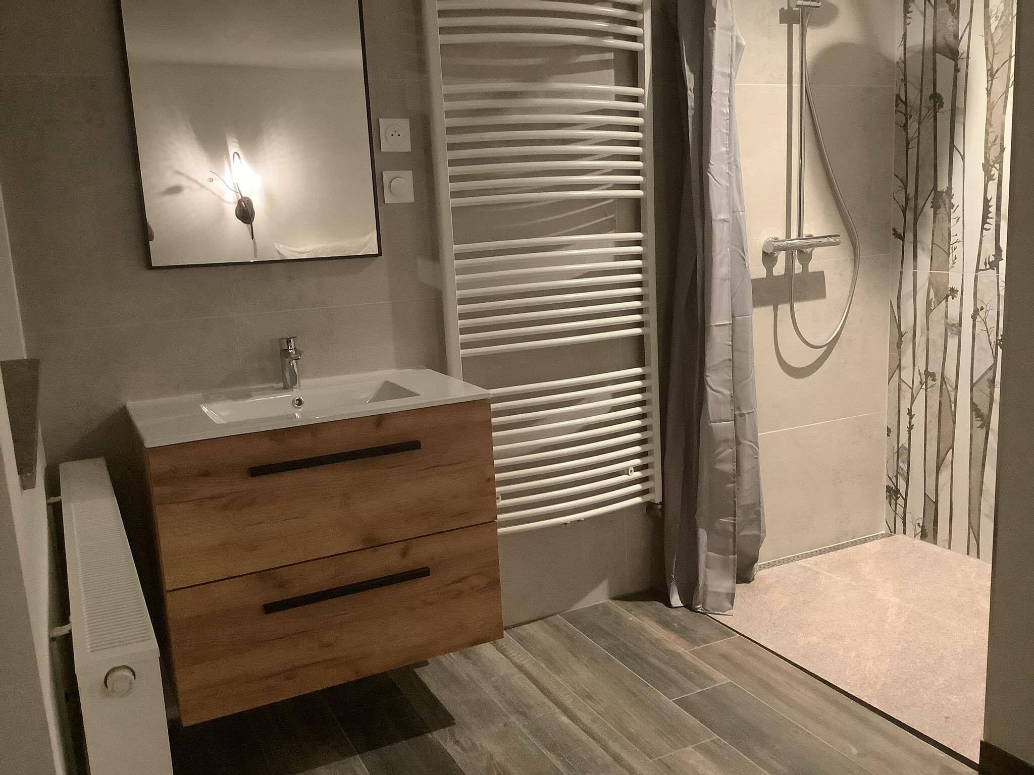 Un baño moderno con tocador de madera, un espejo, ducha con puerta de cristal y una ventana con persianas.