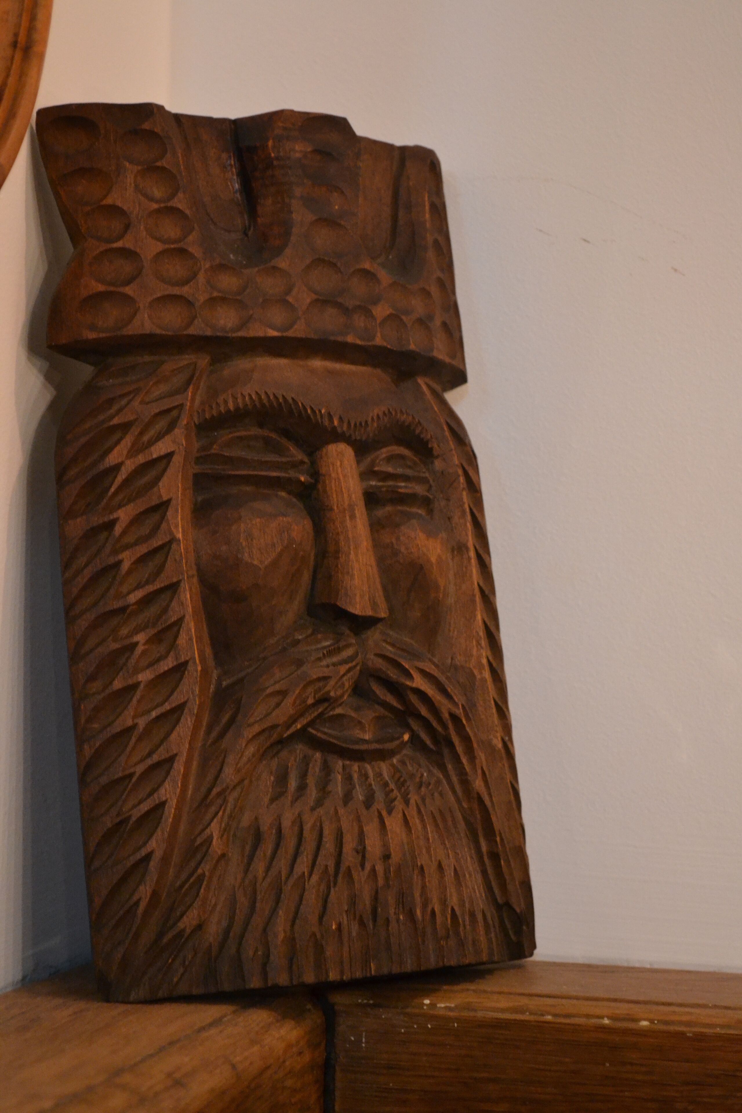 A wooden sculpture with a carved face and a textured top.