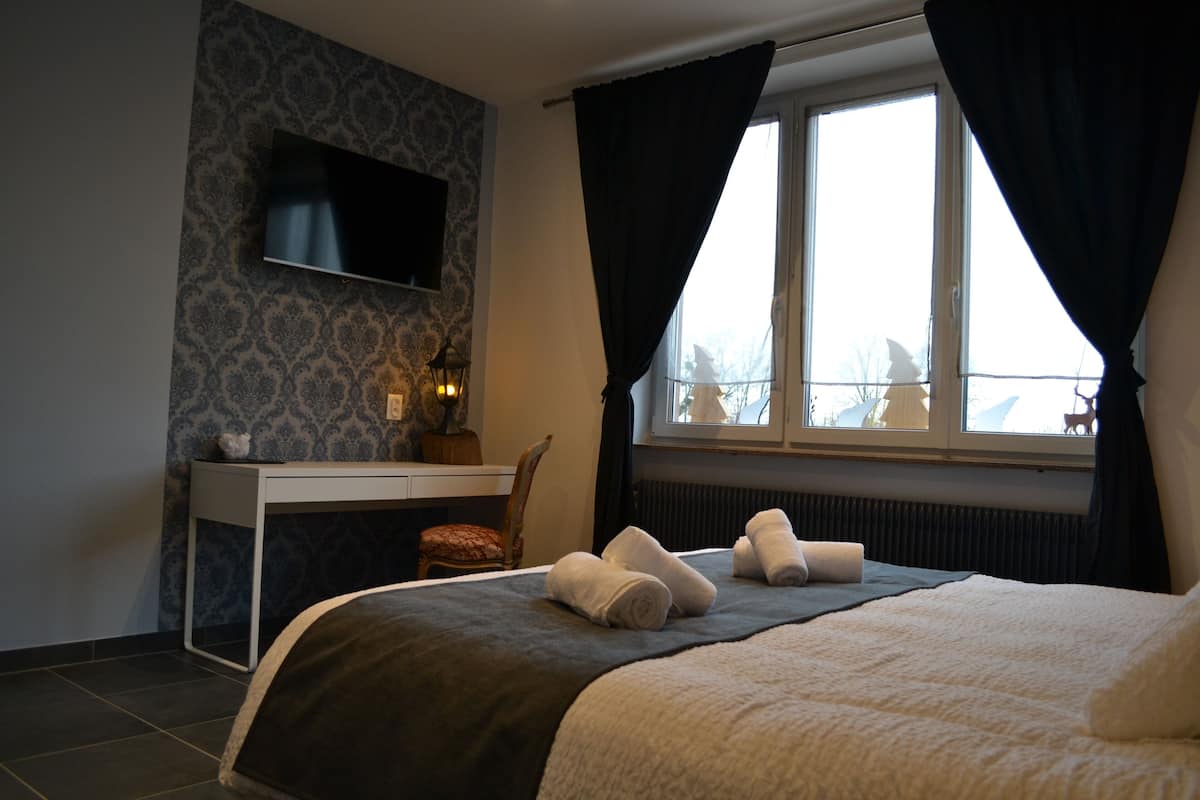 Une chambre d’hôtel équipée d’un lit, d’un bureau, d’une chaise, d’un téléviseur fixé au mur et d’une fenêtre avec des rideaux.