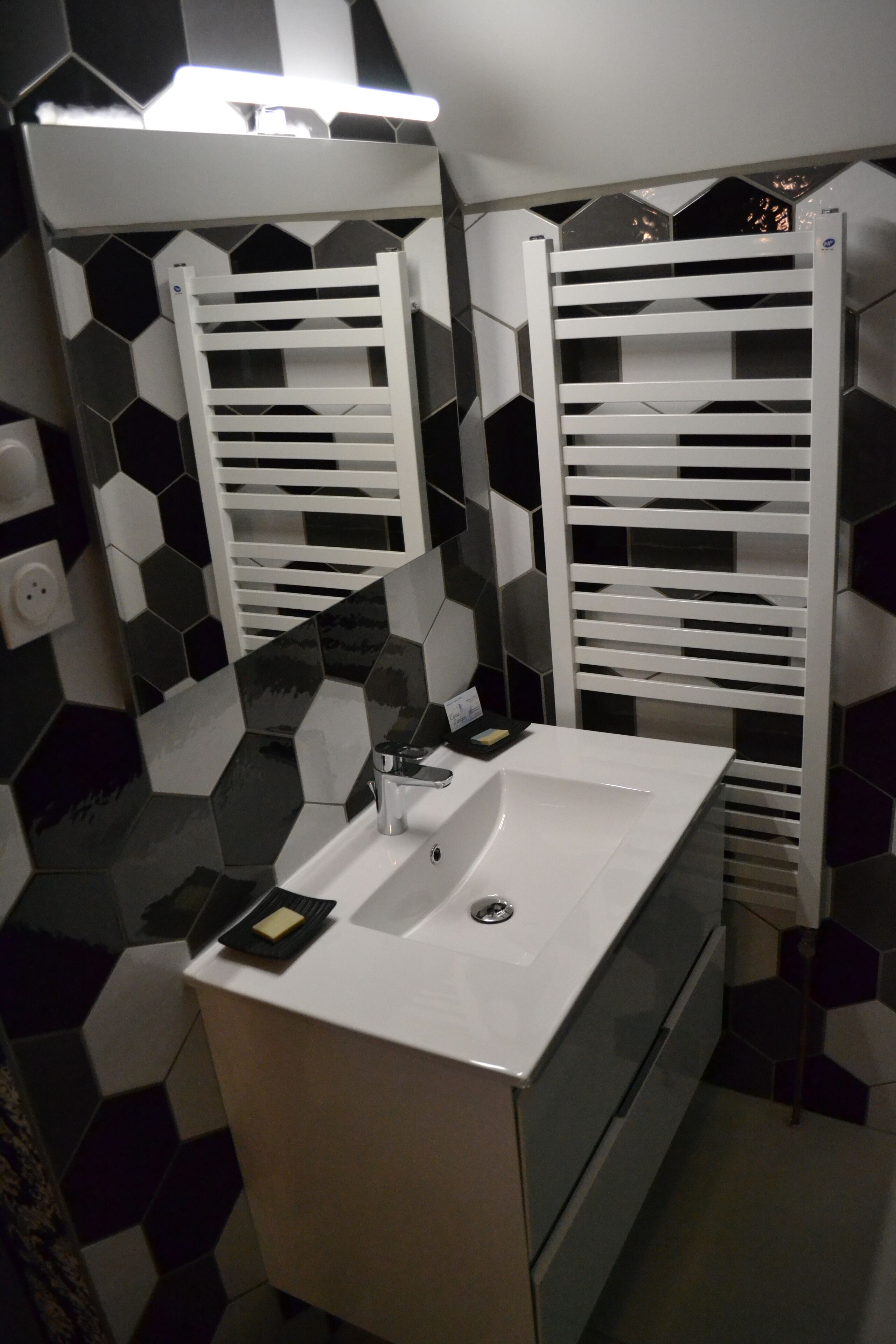 A bathroom with a white sink, a mirror, and a towel rack. The wall has a black and white hexagonal tile pattern.