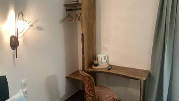 A corner room with a wooden desk, a chair, a wall-mounted light, a plant, and a small shelf.