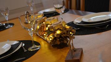 Una mesa de comedor dispuesta con platos, cubiertos y copas de vino, con un centro decorativo de velas y leña.