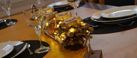 A dining table set with plates, cutlery, and wine glasses, with a decorative centerpiece of candles and logs.