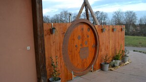 Une porte en bois rustique, de forme circulaire et de grande taille, agrémentée de plantes en pot et surmontée d’une structure métallique.