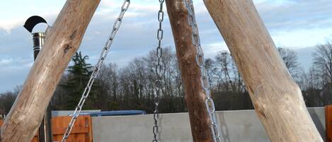A metal hot tub suspended by wooden beams and chains.