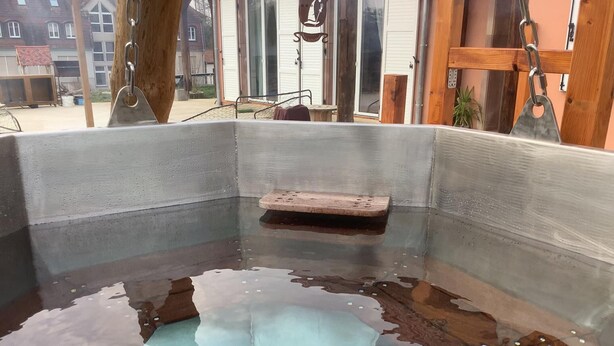 Un bain thermal en plein air, avec un banc en bois et des garde-corps en métal.