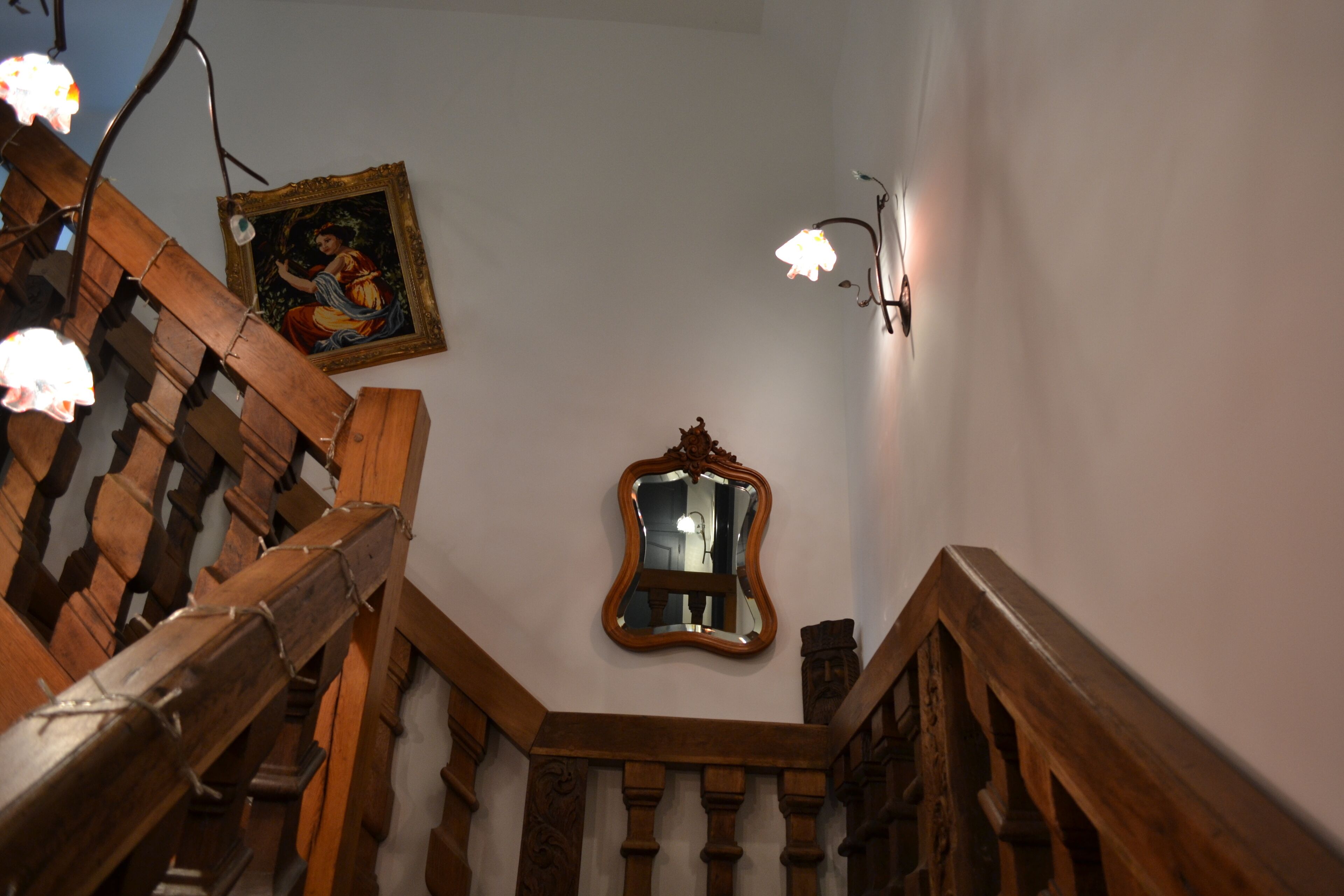 Un escalier en bois avec une rampe, un miroir fixé au mur et un tableau encadré.