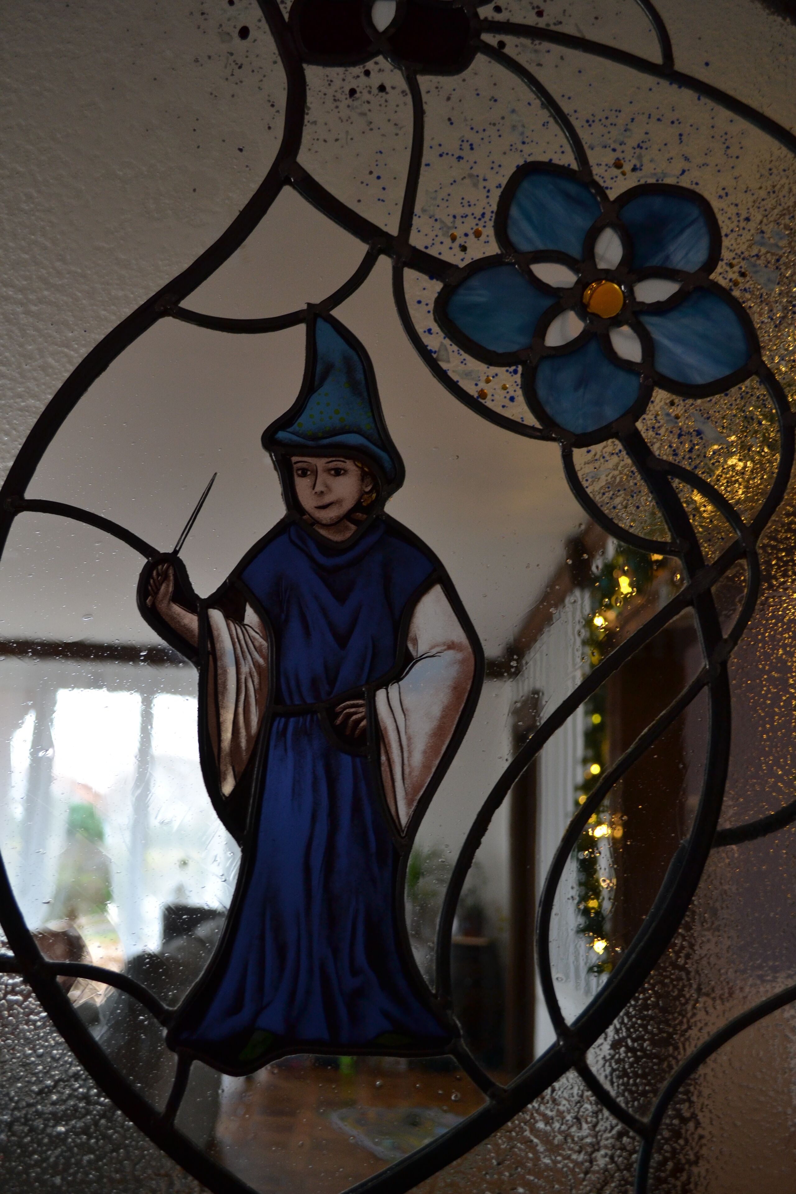 A stained glass window with a figure holding a staff, surrounded by floral patterns.