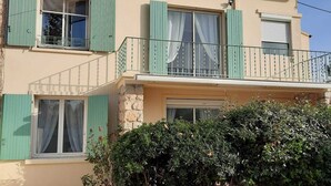 Un bâtiment à deux étages, avec des volets verts, un rez-de-chaussée en pierre et une allée gravillonnée.