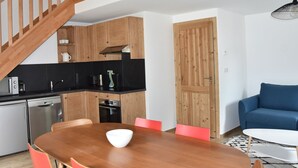 Une cuisine moderne avec des meubles en bois, un plan de travail noir et un coin repas comprenant une table en bois et des chaises rouges.