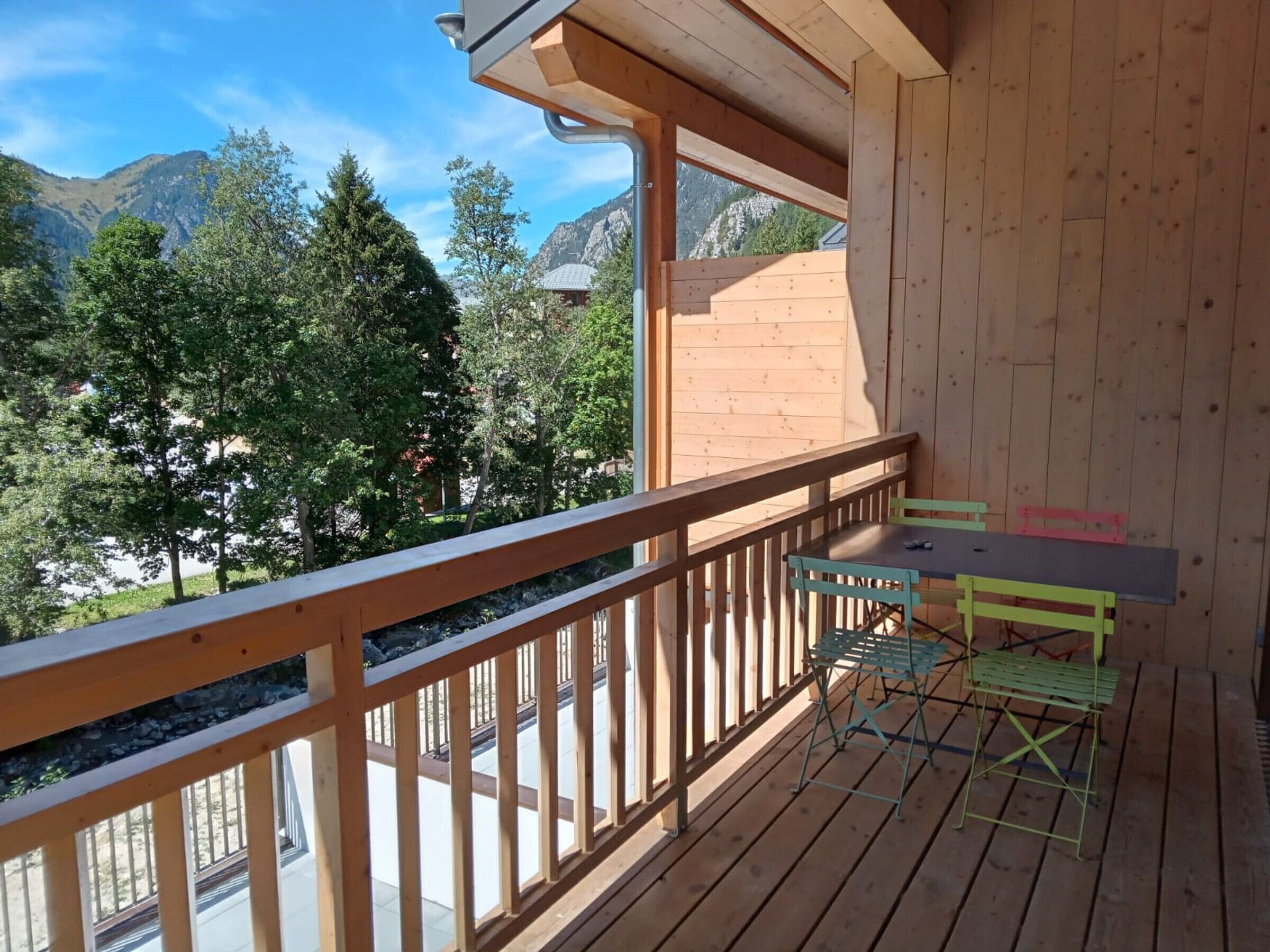 Eine Holzterrasse mit Tisch und Stühlen, mit Blick auf eine gebirgige Landschaft.
